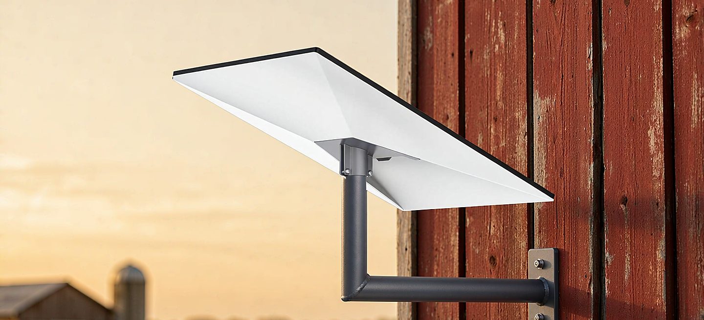 A Starlink dish on a wall bracket mounted on weathered red barn siding at golden hour