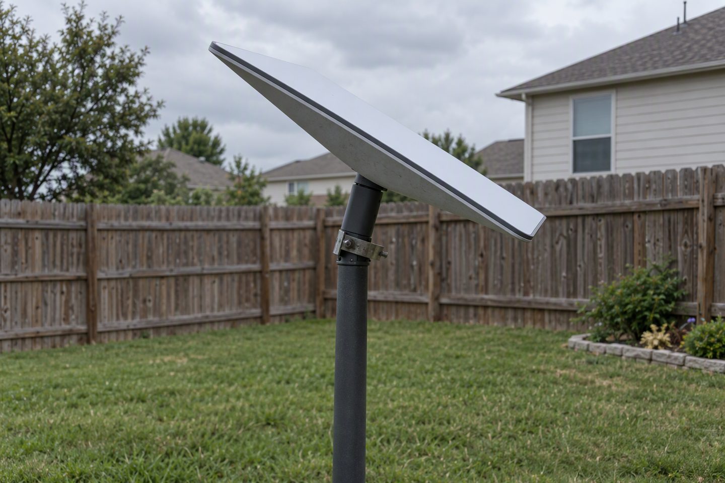 A rectangular Starlink-style panel on a pole mount that has slipped and tilted out of alignment, the mast clamp visibly loose on the pipe