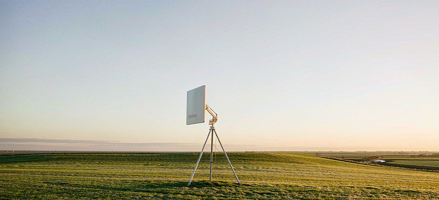 A Starlink dish on a freestanding tripod on open grass, showing a portable setup