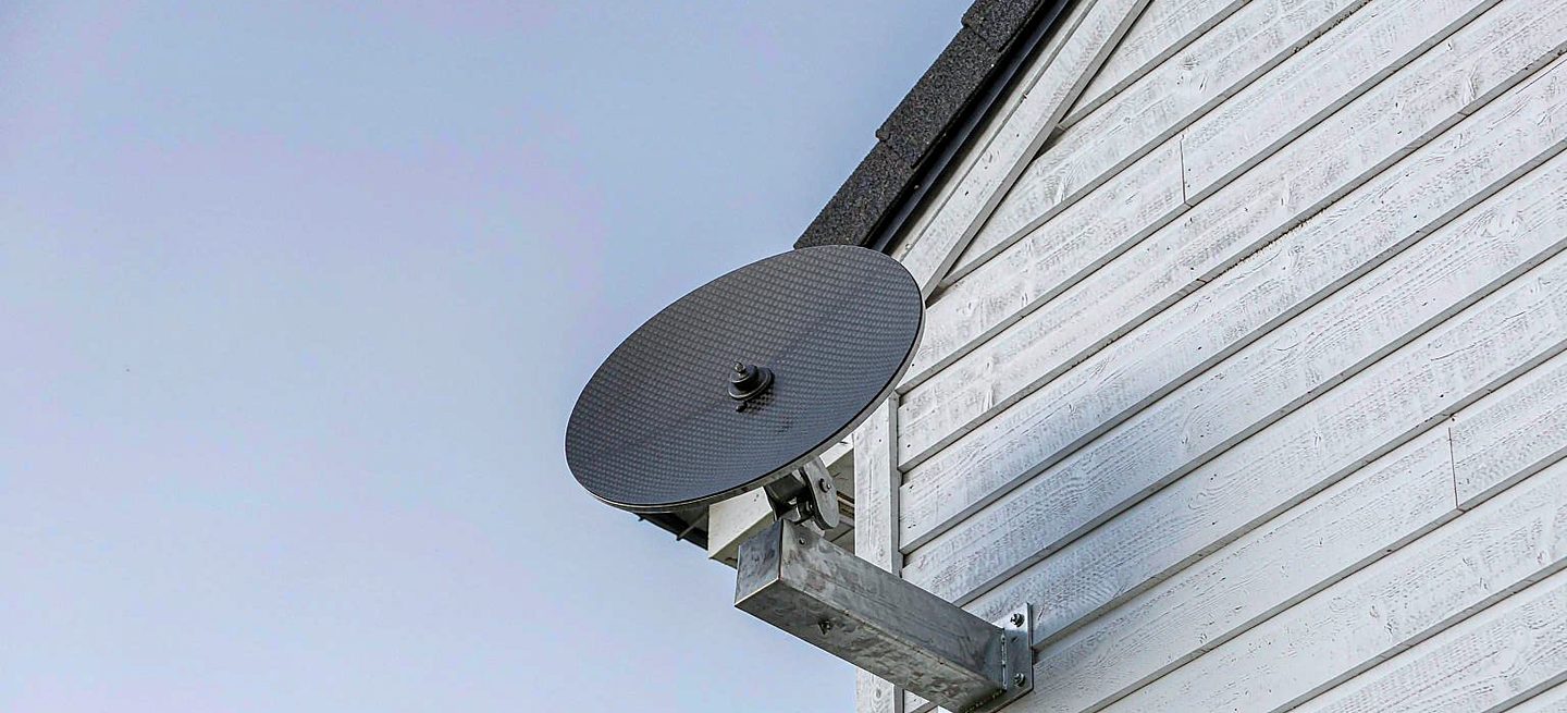 A Starlink dish on a wall bracket beside a house, clear of the roofline